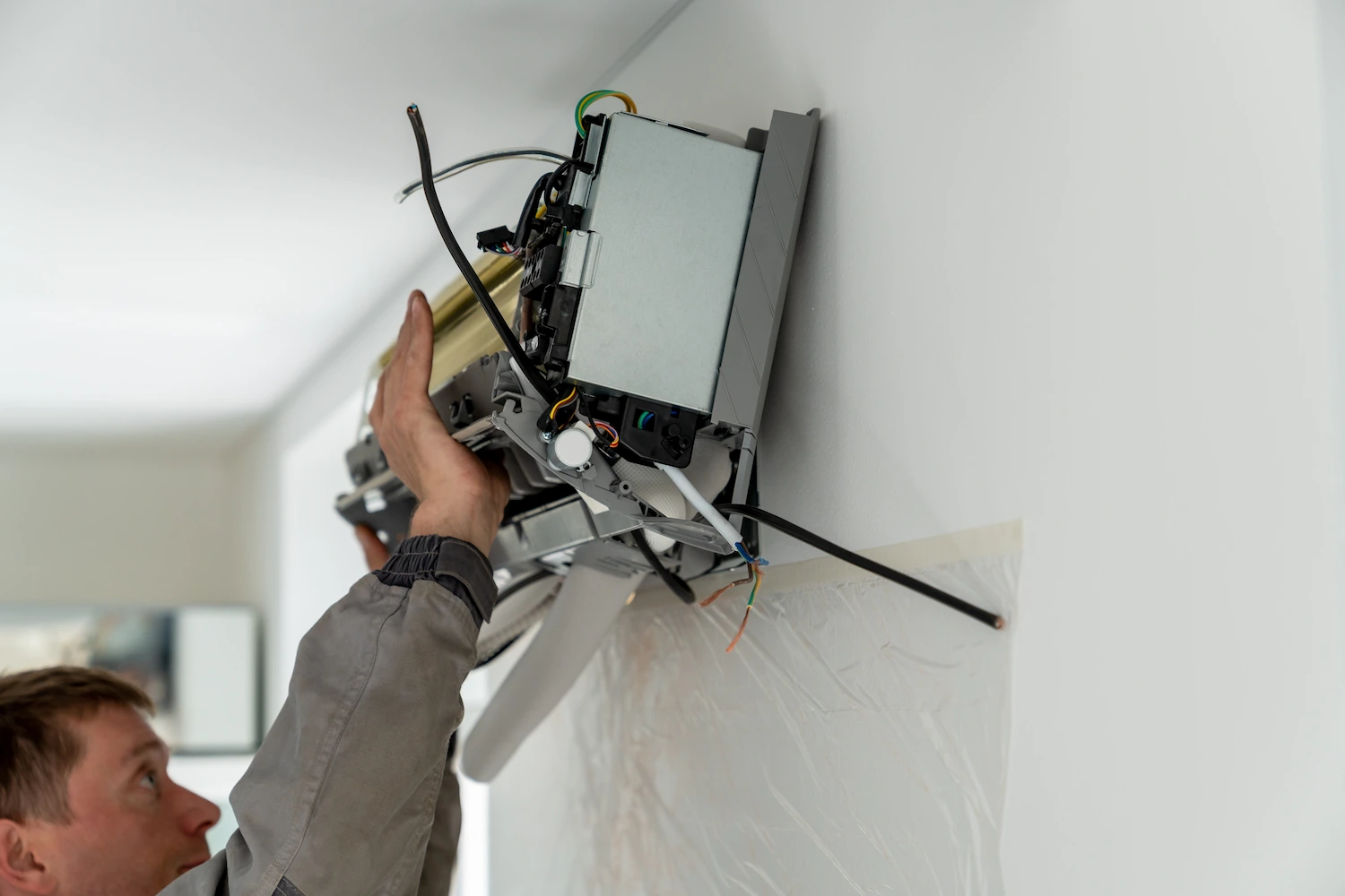 Man technician worker in uniform fixing repairing apartment air conditioner, installing wall-mounted mini split