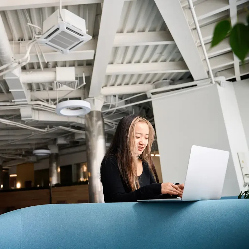 a woman sitting at a blue couch using a laptop